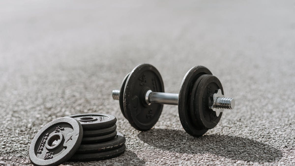 Modern adjustable dumbbell with stainless steel bar and cast iron plates on asphalt road with shadows